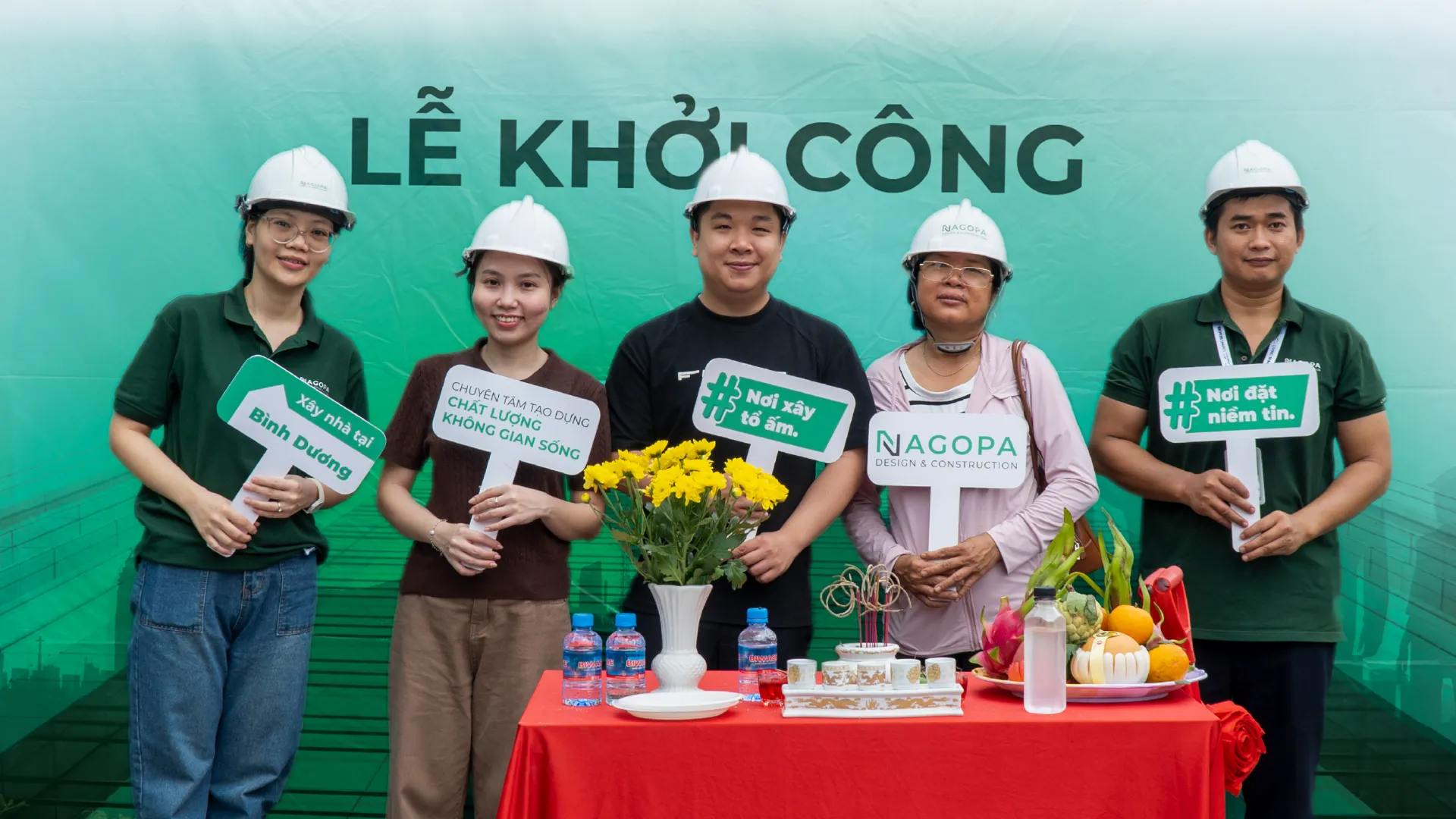 ập thể đội ngũ NAGOPA cùng gia đình chủ đầu tư và người thân rạng rỡ, tay cầm bảng hashtag biểu trưng cho tinh thần "Nơi xây tổ ấm - Nơi đặt niềm tin" của công ty tại Phường Bình Dương.